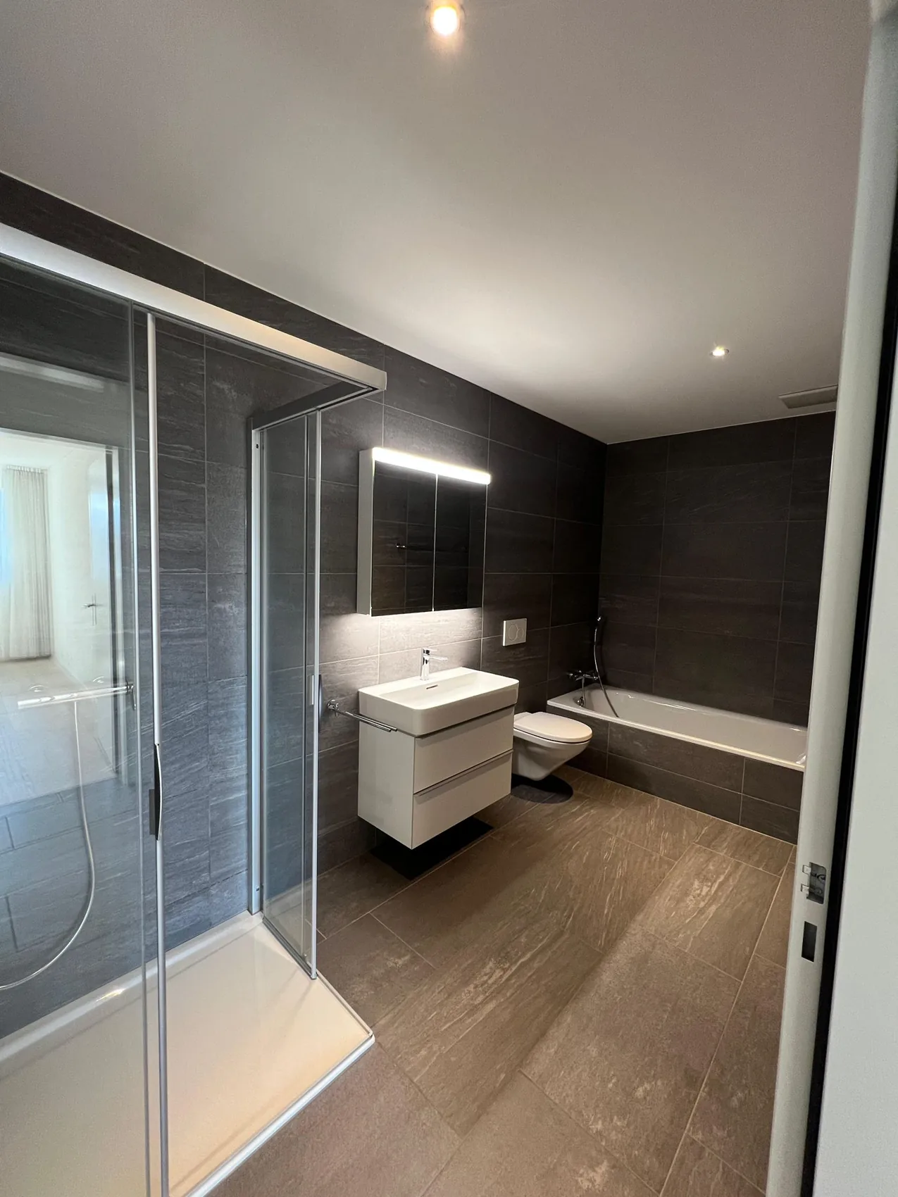 Badezimmer mit dunklen Platten und Glasdusche